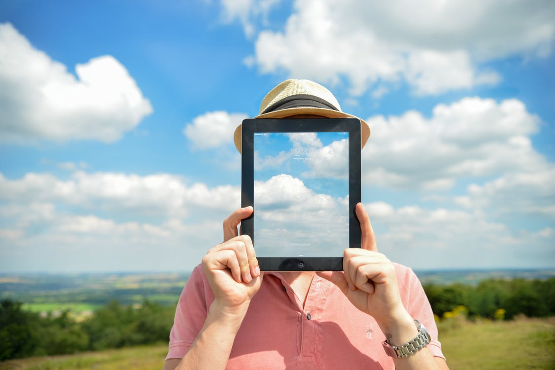 A person holding a tablet pc with a picture of clouds over their face