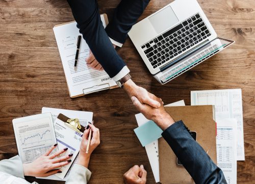 Xero Payroll People shaking hands across a laptop and files.
