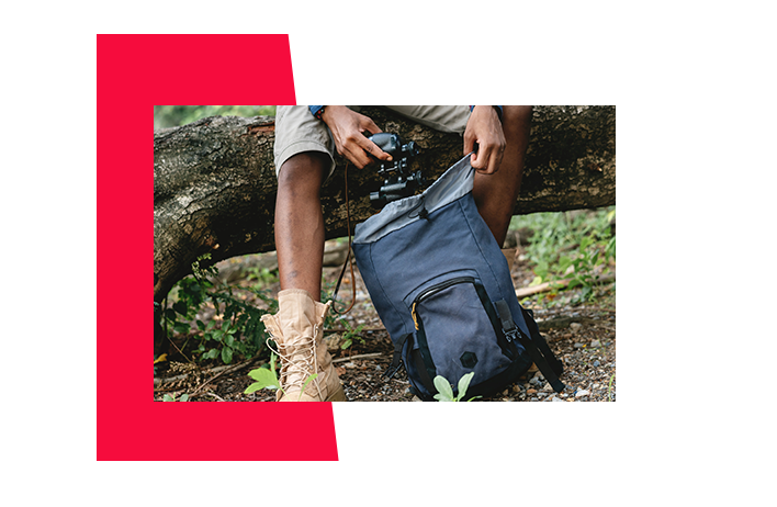 A person grabbing a camera out of their backpack within a woodland area