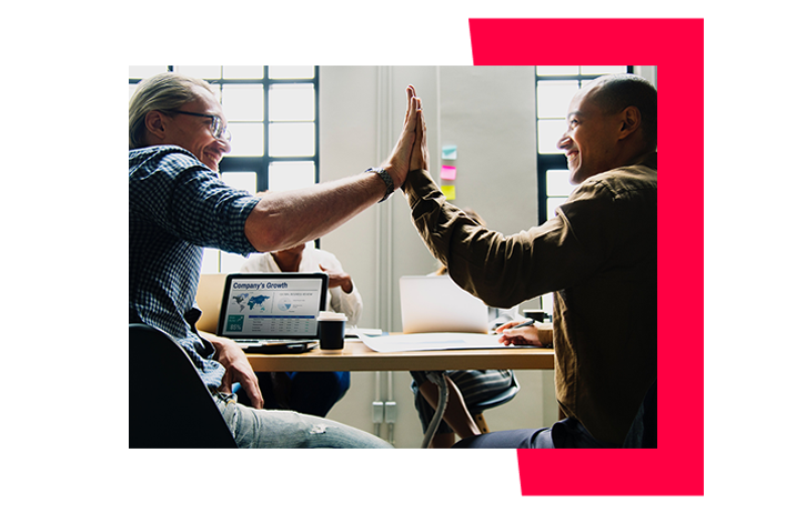 Two men sitting at a desk high-fiving